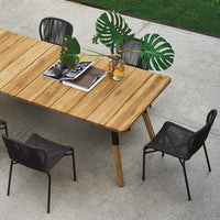 "Natural wood table with sleek black chairs and green plant accents on a textured concrete surface."