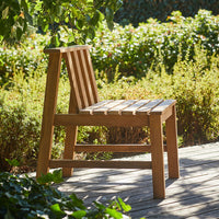 Natural wooden chair with a slatted design, featuring a warm brown finish amidst a lush green garden backdrop.
