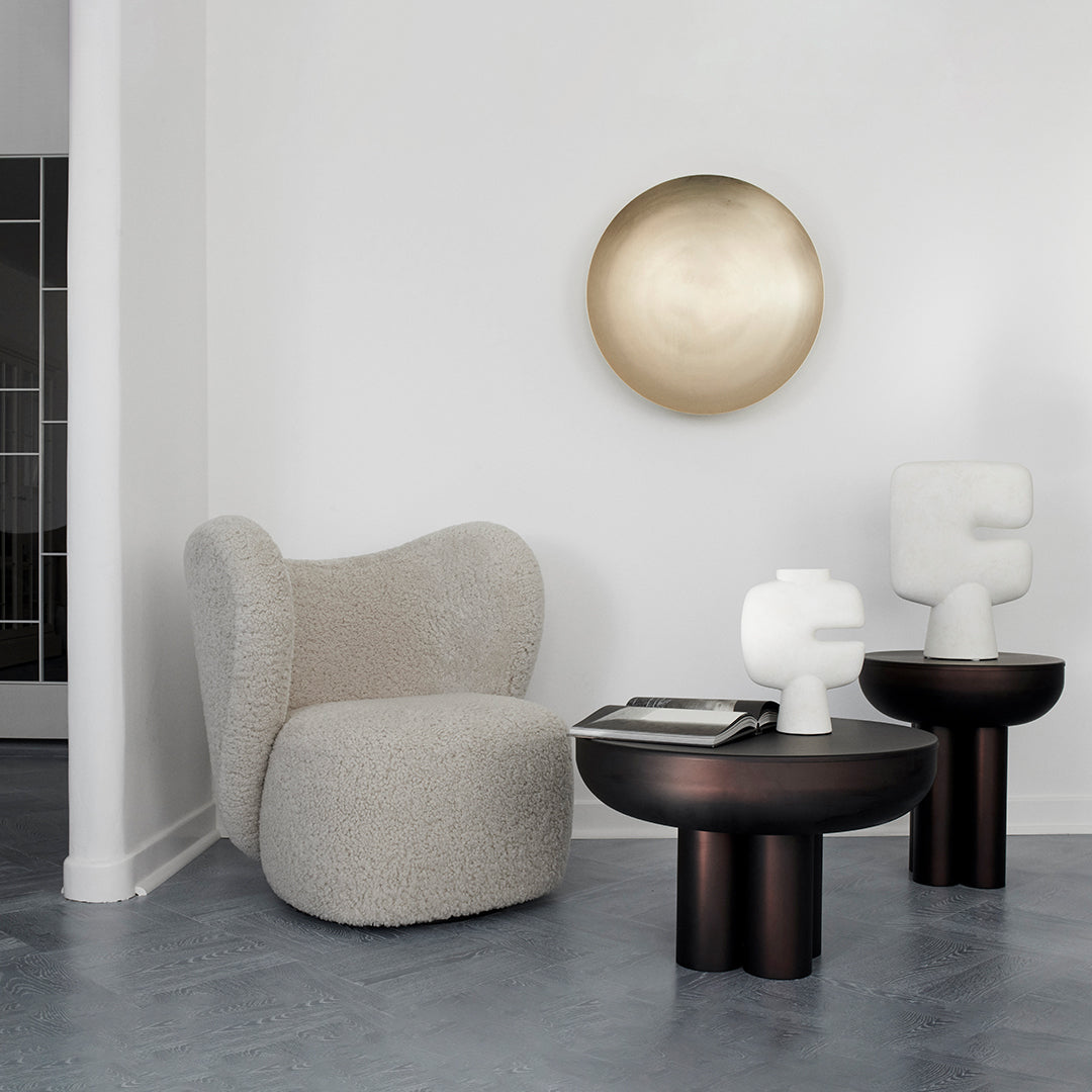 Cream and beige patterned chair with black and white accent tables, gold wall art, and a muted gray floor.