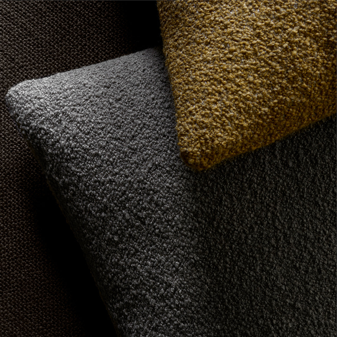 Textured fabric swatches in dark gray, warm gold, and rich brown hues, showcasing elegant patterns and finishes.