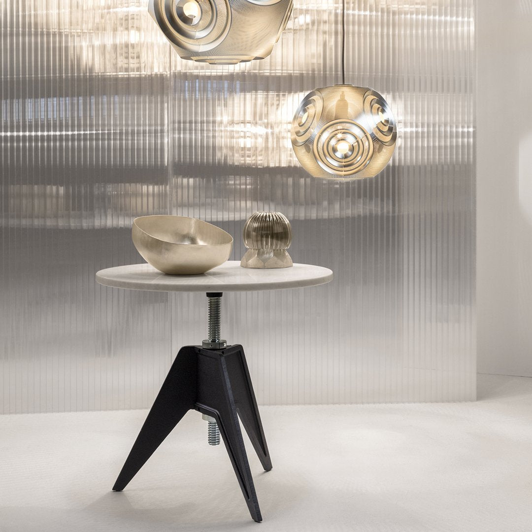 Modern round table with a white top and black tripod legs, complemented by metallic decor and a textured gray background.