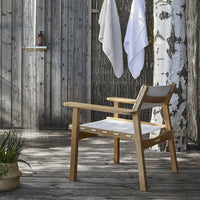 Minimalist wooden chair with a natural finish and white fabric seat, set against a rustic outdoor background.