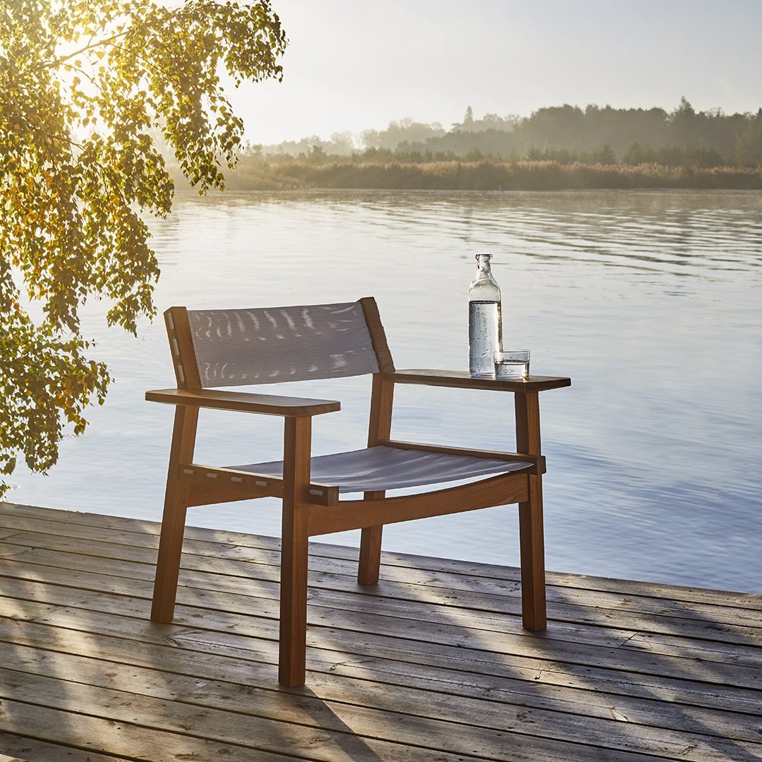 Brown wooden chair with slatted backrest against a serene lake backdrop, featuring warm sunlight and soft natural hues.