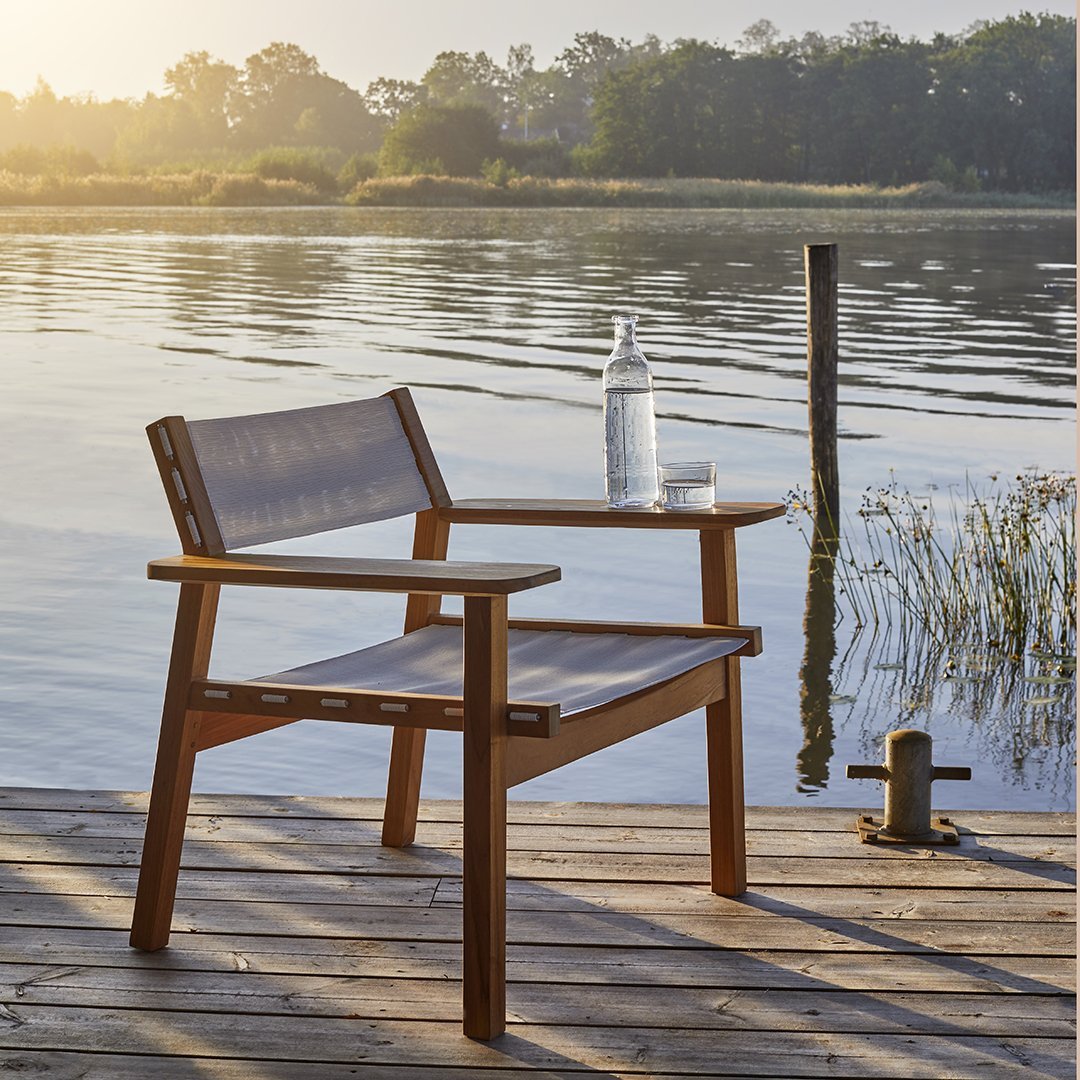 Wooden chair with a light gray fabric seat and backrest, set against a tranquil lakeside backdrop.