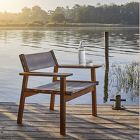 Wooden chair with a light gray fabric seat and backrest, set against a tranquil lakeside backdrop.