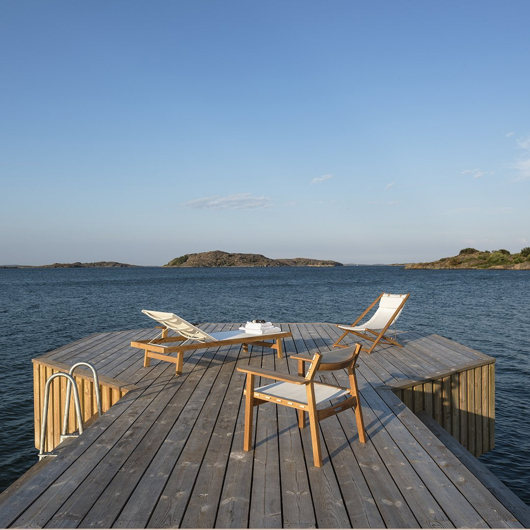 "Light wood patio furniture on a wooden dock, featuring blue water and a clear sky backdrop."