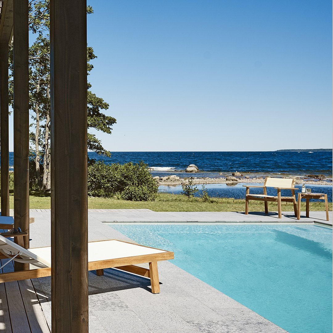 "Relaxing poolside scene with clear blue water, green grass, and a serene coastal view."
