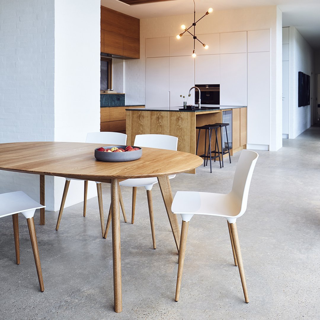 Modern wooden dining table with light wood legs and white chairs against a neutral-toned interior.