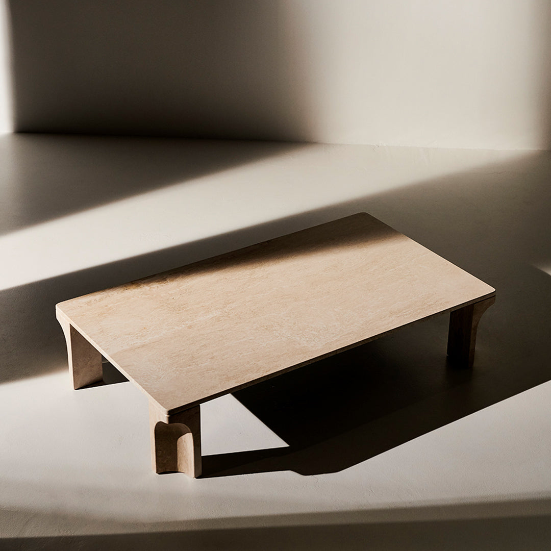Light beige table with smooth, minimalist design and subtle surface texture, set against a soft, shadowy background.