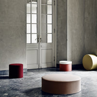 Colorful fabric stools in red, yellow, and beige with solid patterns against a gray backdrop and natural light.
