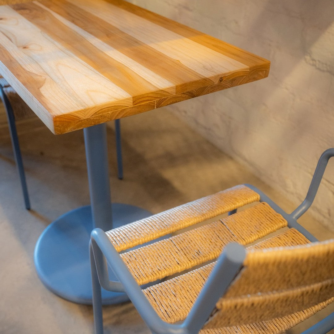 Light wood tabletop with natural grain, paired with a blue metal base and woven beige seat. Modern and stylish design.