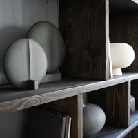 Unique geometric vases in soft gray and cream hues, showcased on a rustic wooden shelf with a dark finish.