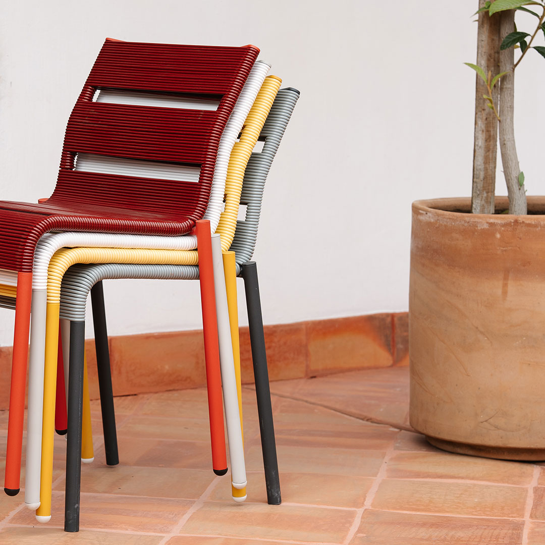 Stack of colorful chairs featuring red, yellow, gray, and black stripes against a terracotta floor and pot.
