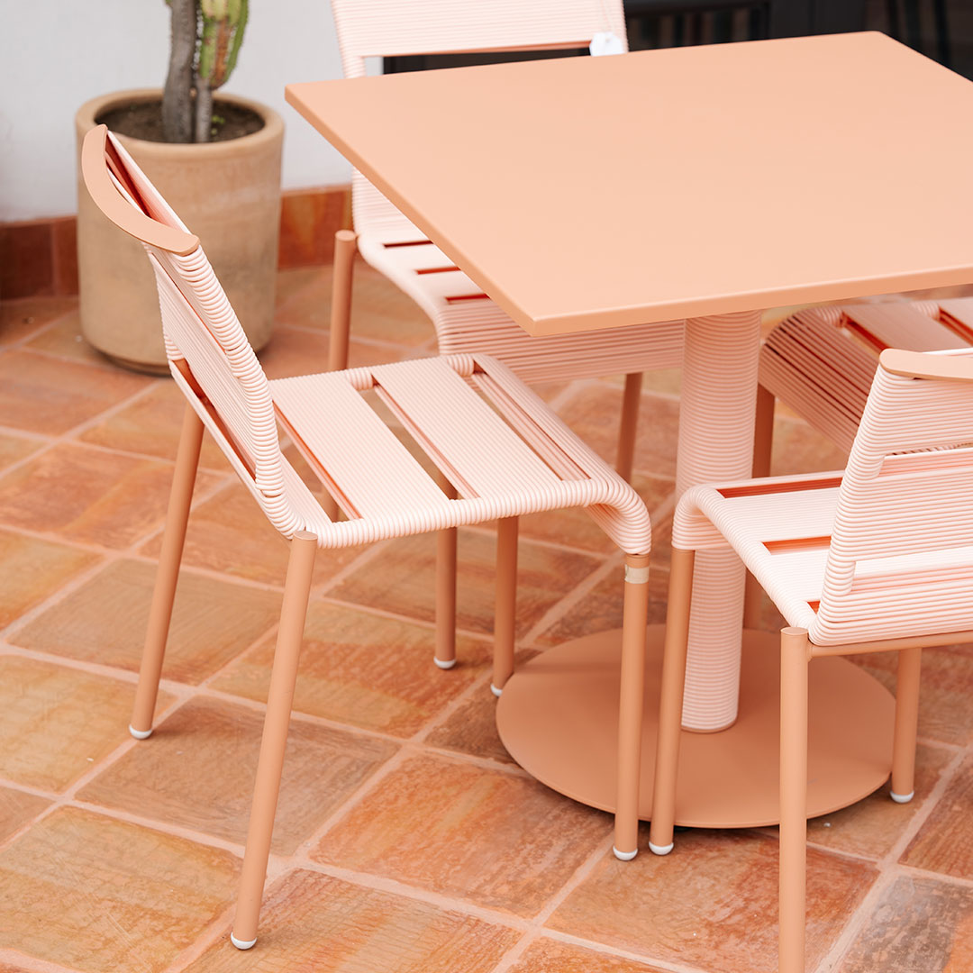 Peach-colored dining set with sleek lines, featuring a square table and matching slatted chairs on tiled floor.