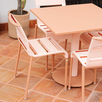 Peach-colored dining set with sleek lines, featuring a square table and matching slatted chairs on tiled floor.