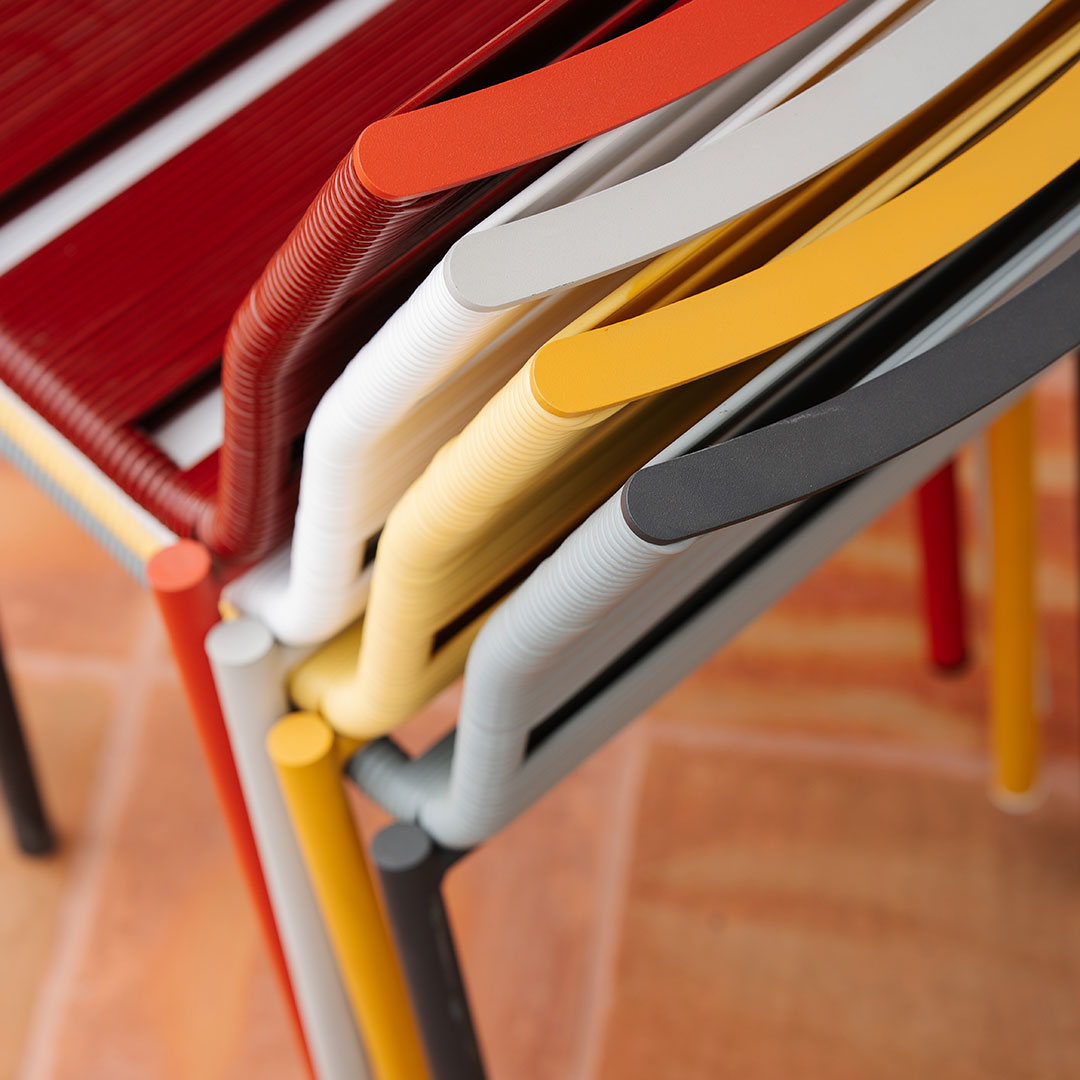 Colorful stacked chairs featuring red, yellow, white, gray, and black patterns against a warm, textured background.