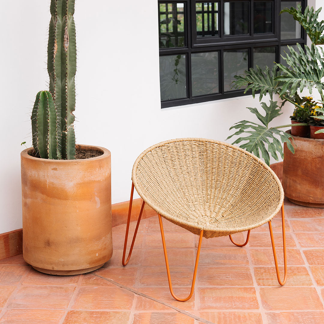 Natural woven rattan chair with a circular design and orange metal legs, complemented by earthy terracotta planters.