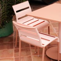 "Elegant blush pink dining chairs with slatted design paired with a smooth round table in a stylish outdoor setting."