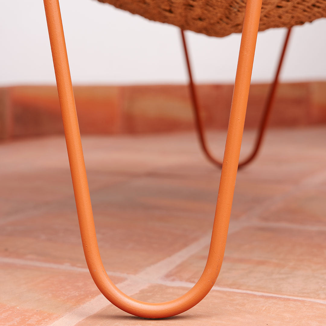 "Close-up of orange metal legs supporting a textured woven basket, set against a warm terracotta tile floor."