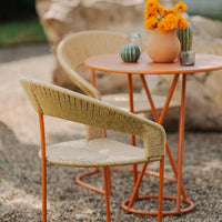 Tan woven chair and orange metal table with floral centerpiece, set against a natural stone background.