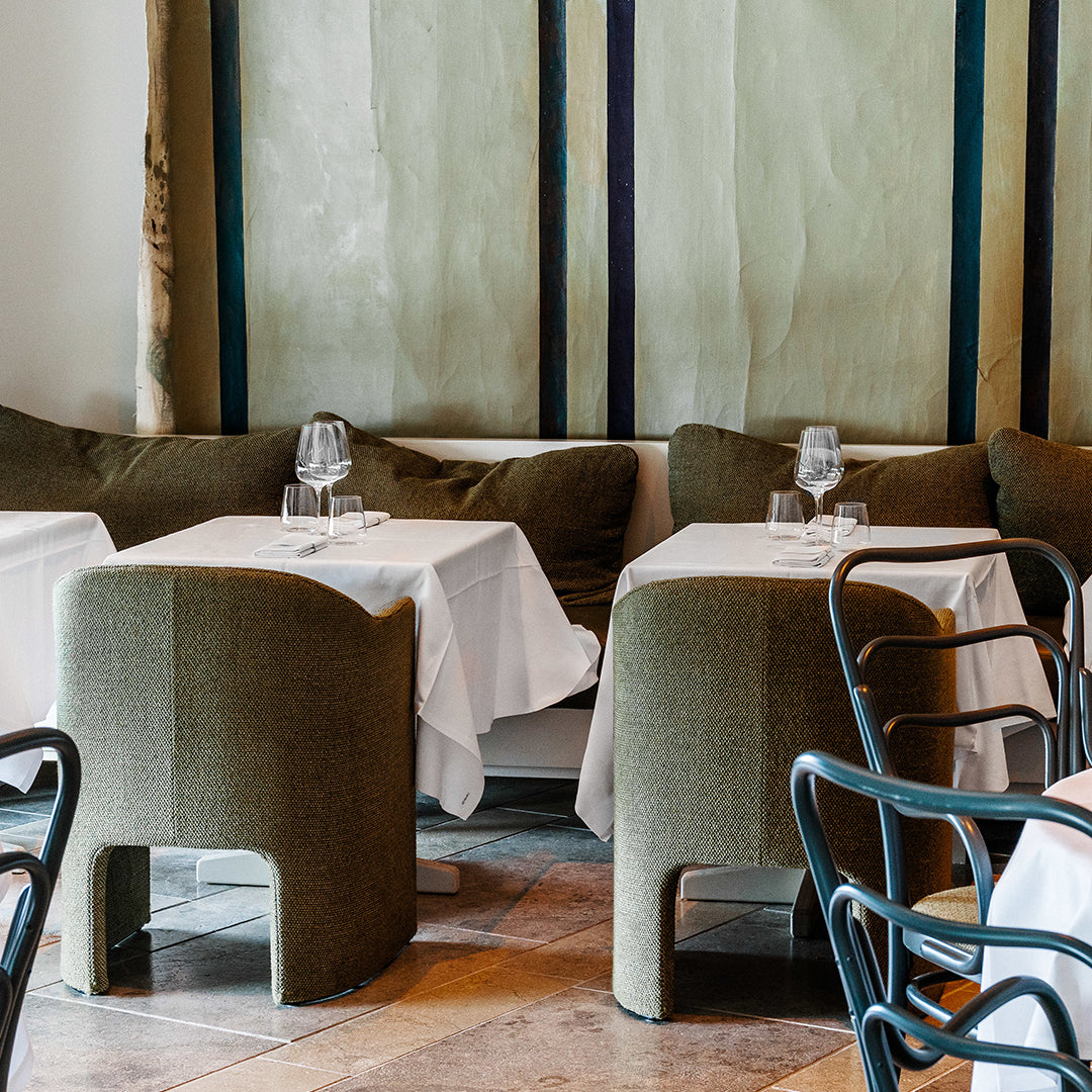 "Stylish green upholstered chairs with white tablecloths in a modern dining space, featuring neutral-toned walls."