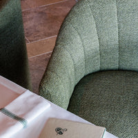 Textured green upholstered chair with a subtle pattern, paired with a white table setting and a beige menu cover.