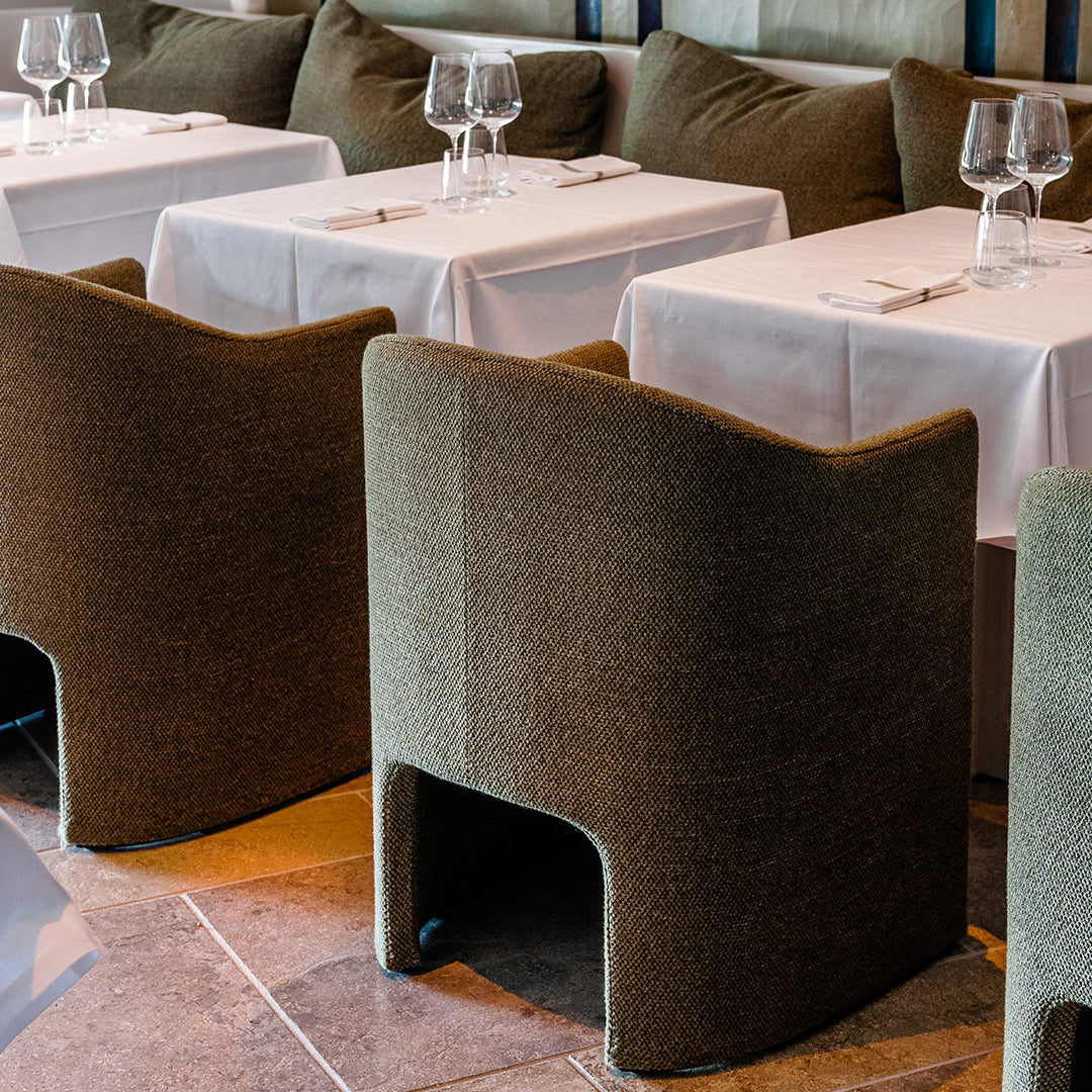 "Textured olive green dining chairs surrounded by elegant white tablecloths in a modern restaurant setting."