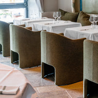 Olive green upholstered chairs with smooth curves, set against a neutral tablecloth and backdrop.