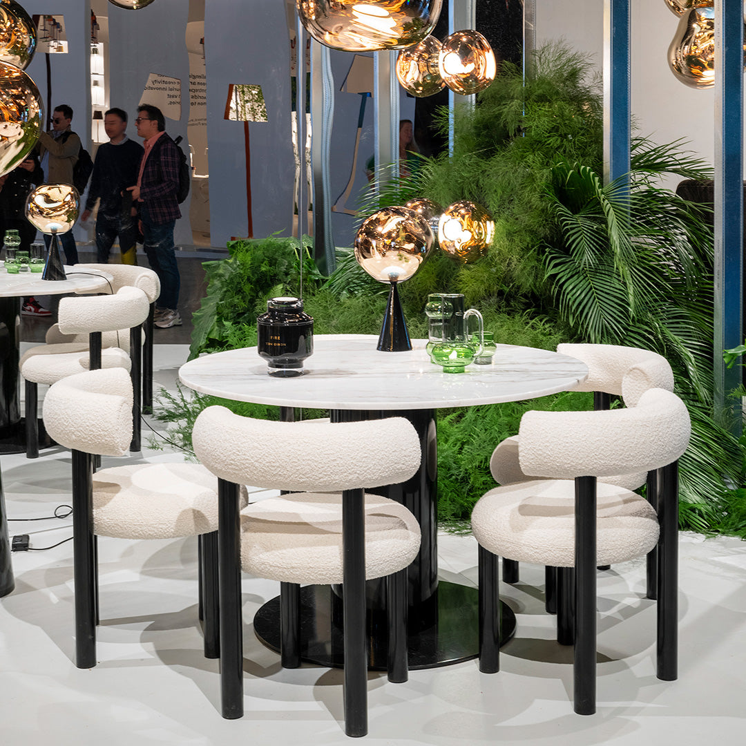 Minimalist round table with a white marble top, surrounded by cream upholstered chairs and black legs. Modern design elements.