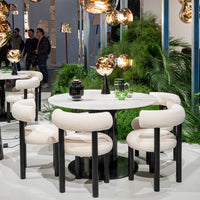 Minimalist round table with a white marble top, surrounded by cream upholstered chairs and black legs. Modern design elements.