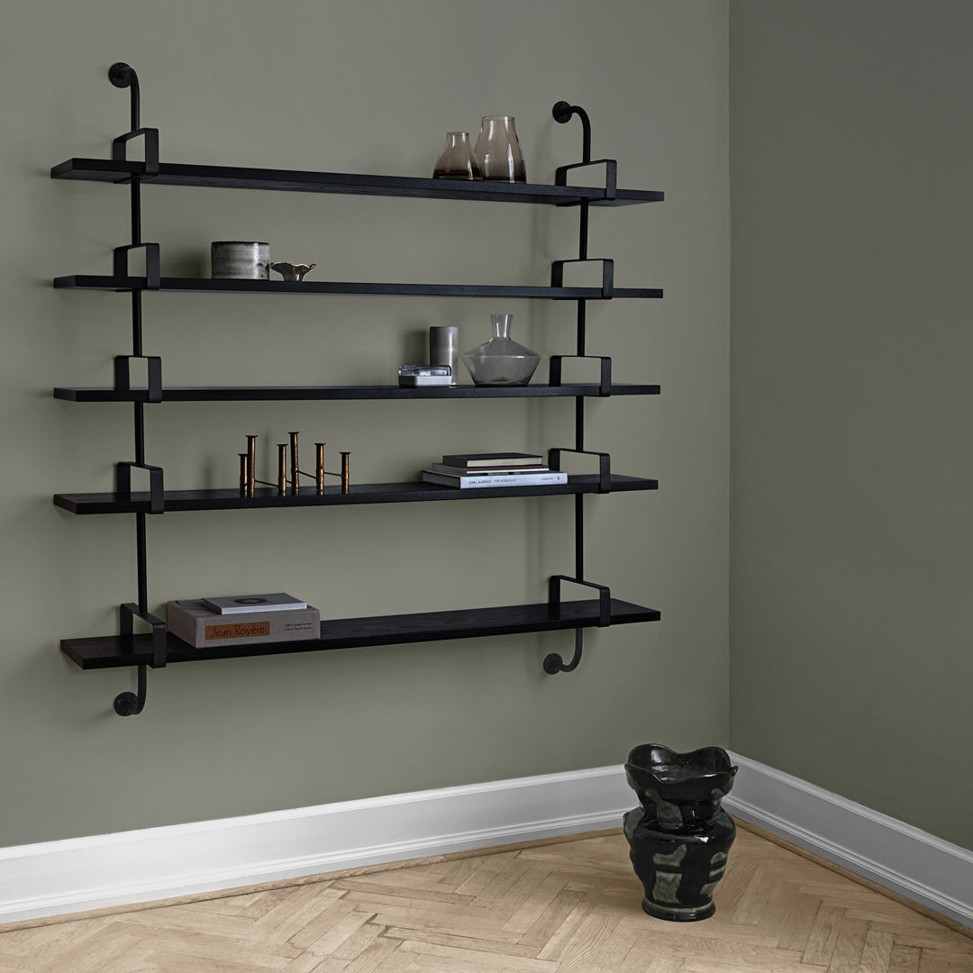 Black metal wall shelves with a sleek design against a muted green wall and light wooden floor.