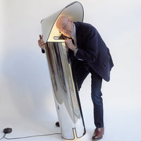Sleek chrome floor lamp with a curved white top and reflective surface, perfect for modern decor.