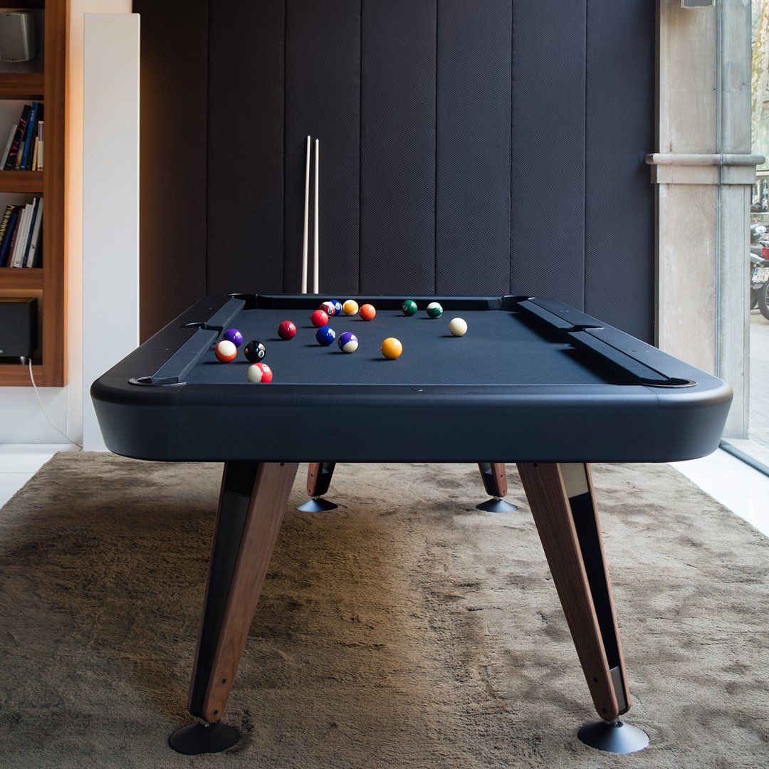 Modern black pool table on wooden legs with colorful billiard balls in various shades on a soft brown carpet backdrop.