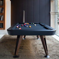 Modern black pool table on wooden legs with colorful billiard balls in various shades on a soft brown carpet backdrop.