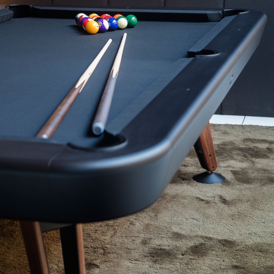 Black pool table with beige felt, two wooden cues, colorful billiard balls in a triangle formation on a textured background.
