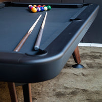 Black pool table with beige felt, two wooden cues, colorful billiard balls in a triangle formation on a textured background.