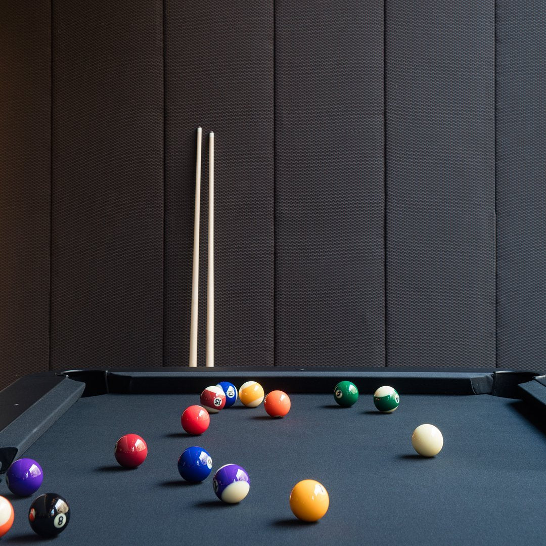 Colorful billiard balls on a sleek black felt table against a textured dark wall, featuring vibrant reds, yellows, and greens.