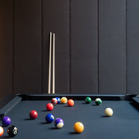 Colorful billiard balls on a sleek black felt table against a textured dark wall, featuring vibrant reds, yellows, and greens.