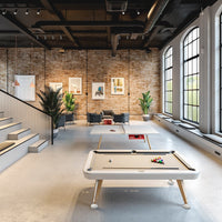 Modern interior with warm brick wall, subtle gray flooring, and a contrasting white pool table accented with colorful balls.
