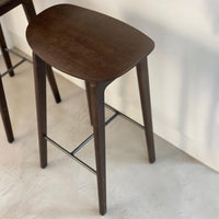 Dark wood bar stool with smooth, rounded top and contrast black metal support. Elegant and minimalistic design.