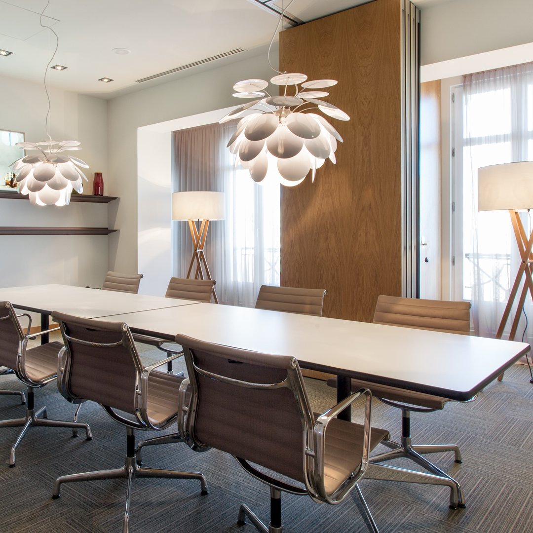 Modern white floral chandelier in a neutral-toned conference room with light wood accents and gray carpet.