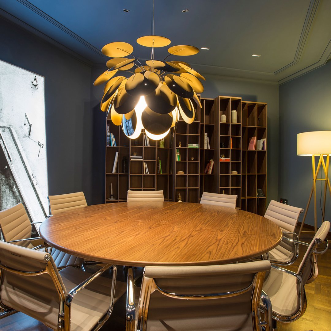 "Modern round wooden table with light oak chairs, warm gold pendant light, and dark blue walls. Stylish and contemporary design."