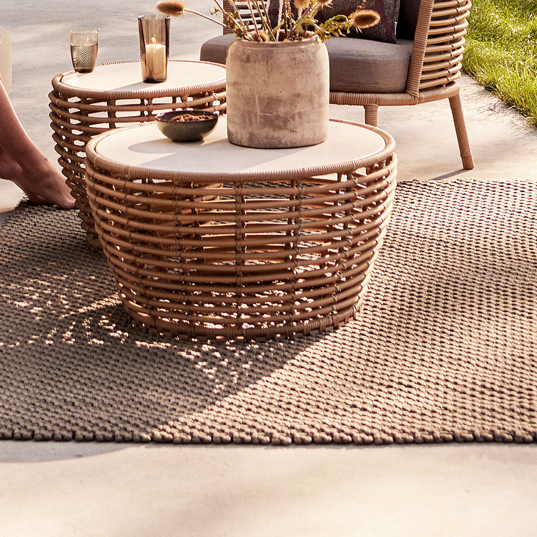 Woven natural rattan coffee tables with cream tops on a textured light gray rug in an outdoor setting.