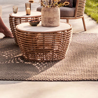 Woven natural rattan coffee tables with cream tops on a textured light gray rug in an outdoor setting.
