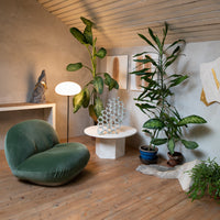 Green velvet lounge chair, white modern table, potted plants, and earthy tones create a stylish interior design scene.