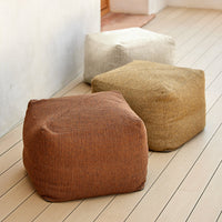 Three cozy poufs in earthy tones: rust, cream, and tan, featuring a textured fabric design on wooden flooring.