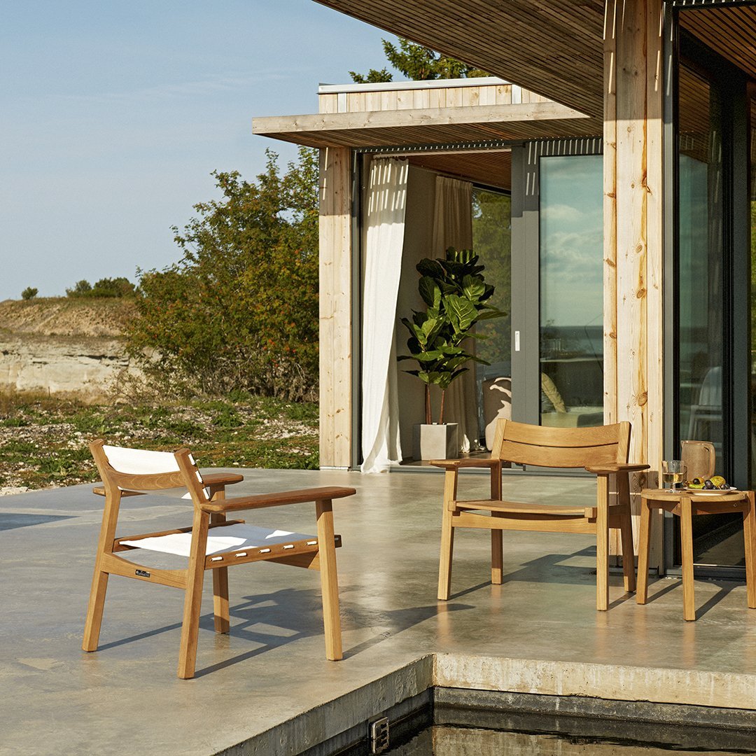 "Natural wood patio chairs in light tones with white fabric accents, set against a serene outdoor backdrop."