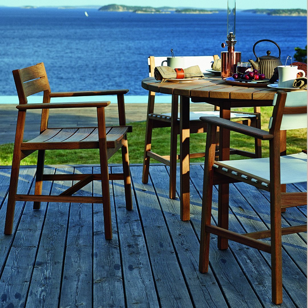 Wooden patio furniture in rich brown tones on a textured wooden deck, with a serene blue ocean backdrop.