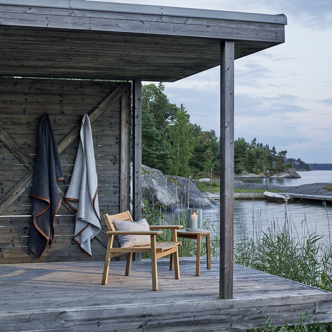 Cozy gray and navy blankets with orange trim, draped on a rustic wooden cabin porch by the water. Perfect outdoor decor.