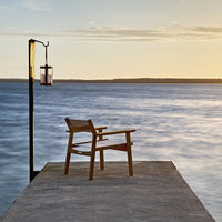 Wooden chair on a dock with warm sunset hues reflecting on calm water, featuring soft blues and golden tones.